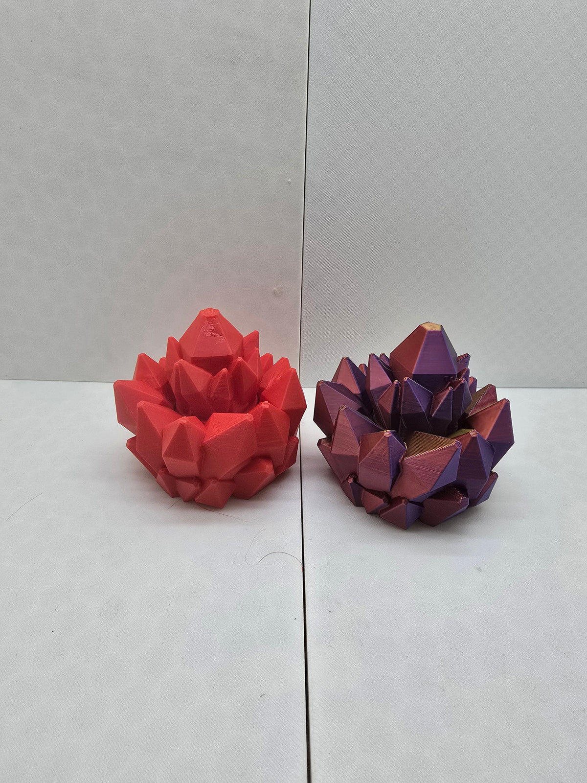 Two 3D printed gemstone fidgets in matte red and iridescent purple-gold silk filament.