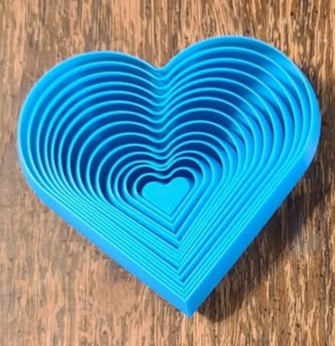 Large blue 3D printed heart fidget with concentric heart-shaped rings on a wooden surface.