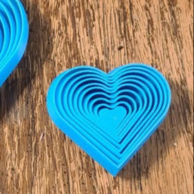 Small blue 3D printed heart fidget with concentric heart-shaped rings on a wooden surface.