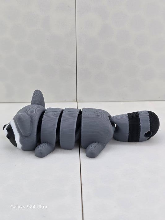3D printed articulated raccoon fidget figure, gray with black and white markings, side view lying flat