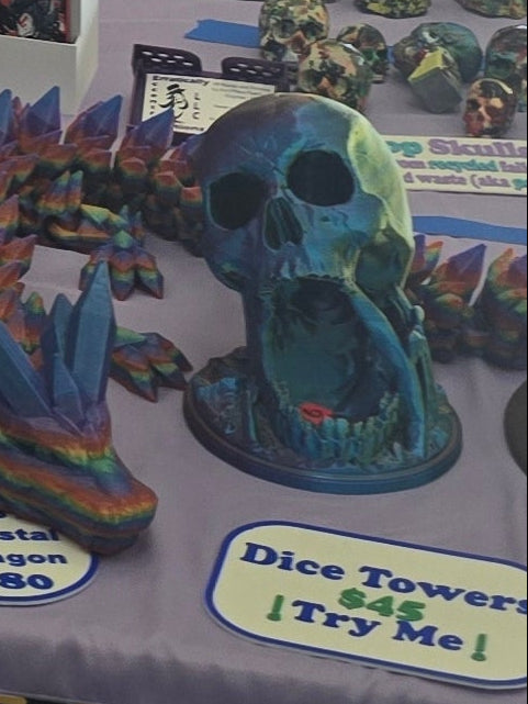 Colorful dice tower with a skull design on a table with promotional text.