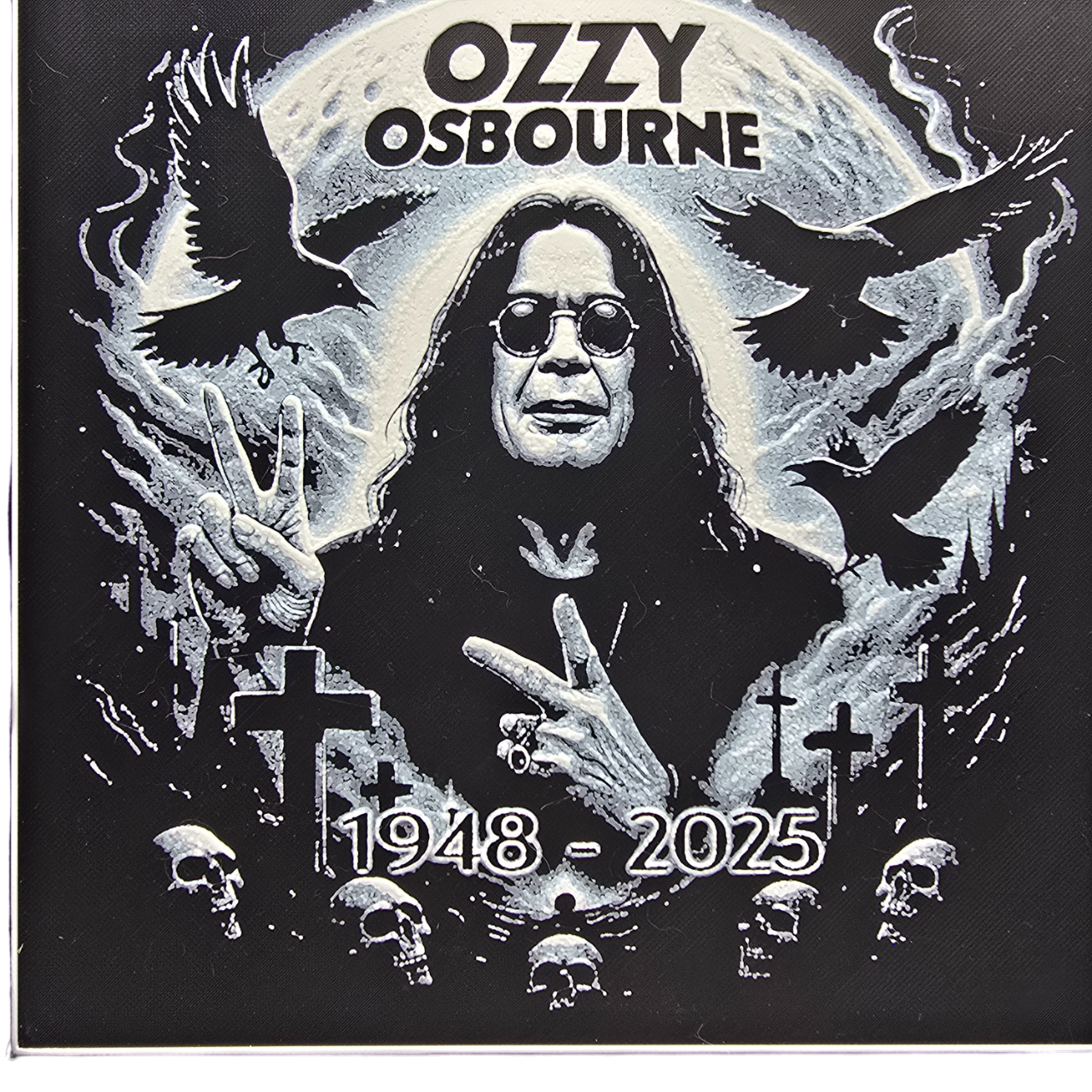 Framed memorial painting for Ozzy Osbourne with crows, skulls, and cross symbols and birth and death years on a black background.