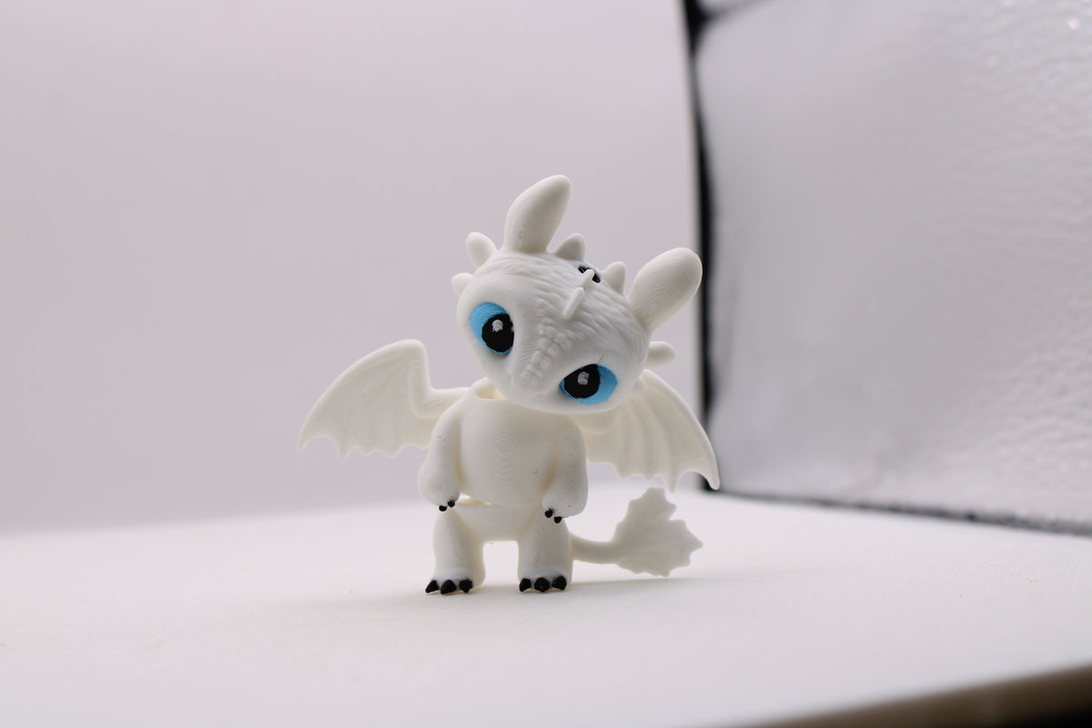 3D printed white Light Fury dragon figurine with blue eyes and black claws on a white background.