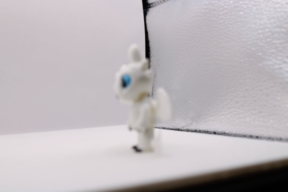 Side view of a white 3D printed Light Fury dragon miniature with blue eyes in a crouched pose.