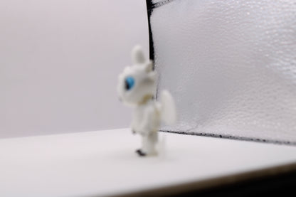 Side view of a white 3D printed Light Fury dragon miniature with blue eyes in a crouched pose.