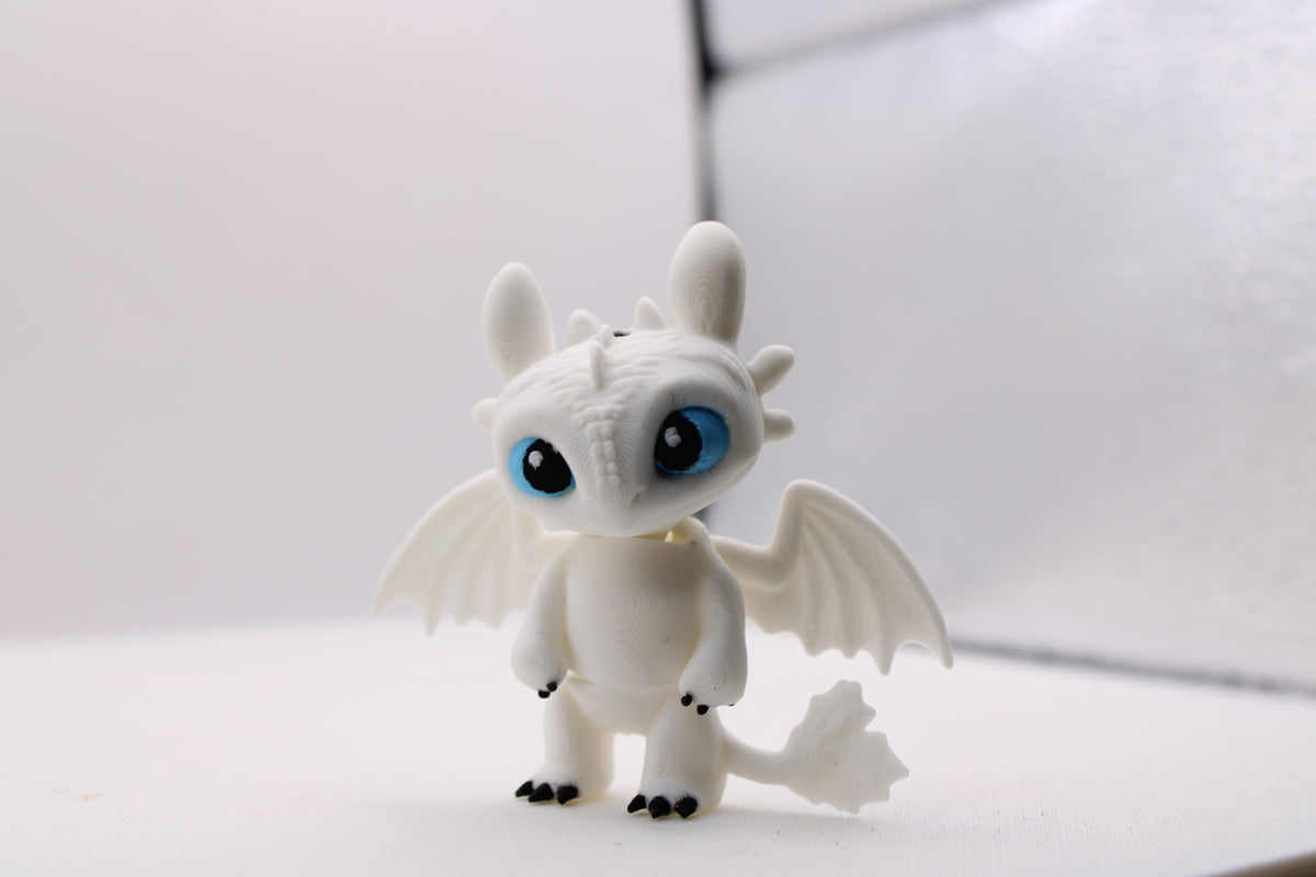 3D printed white Light Fury dragon figurine with blue eyes and black claws on a white background.