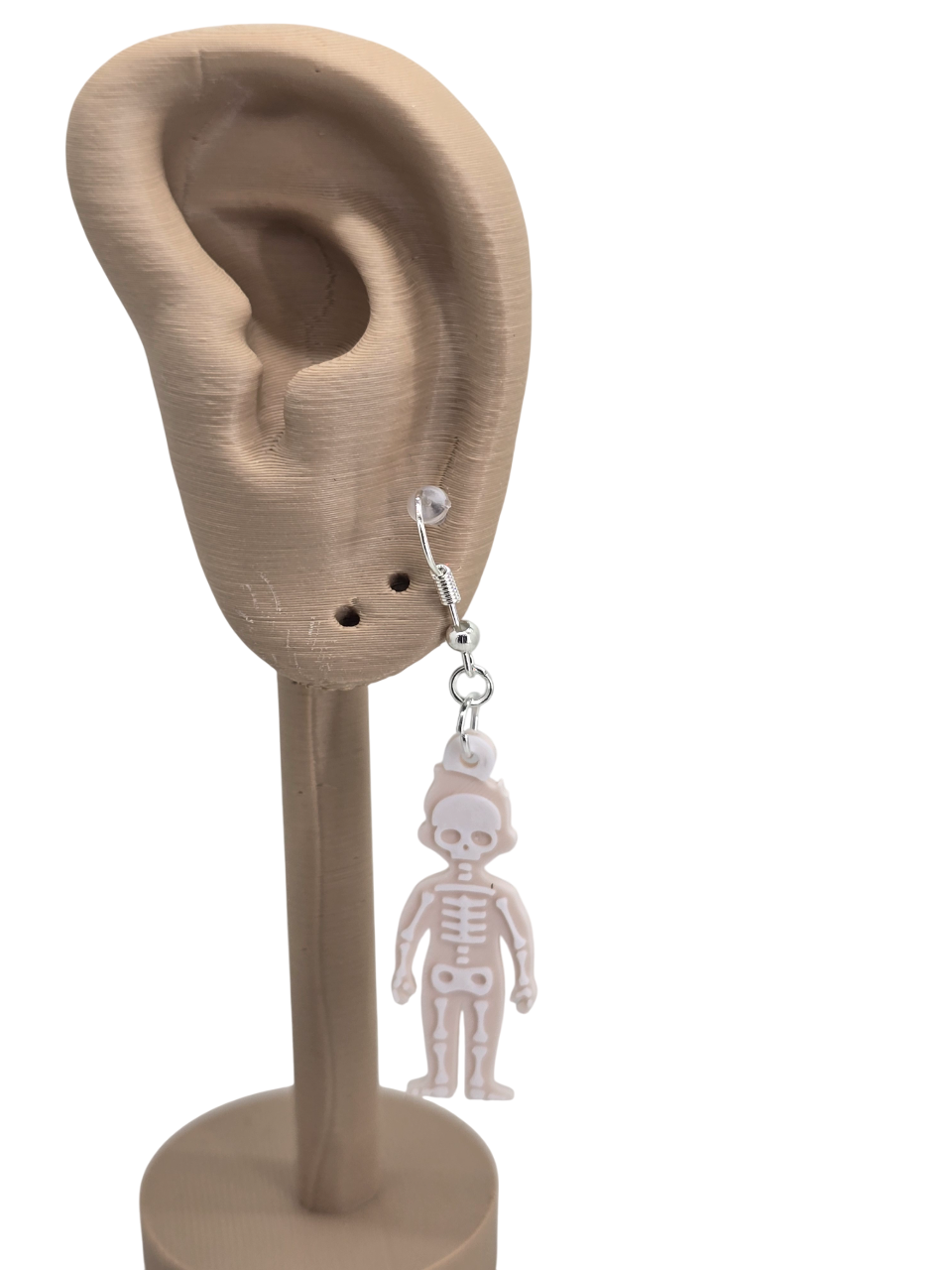 3D‑printed ear model displaying a beige skeleton earring with white layered bone details on a metal hook.