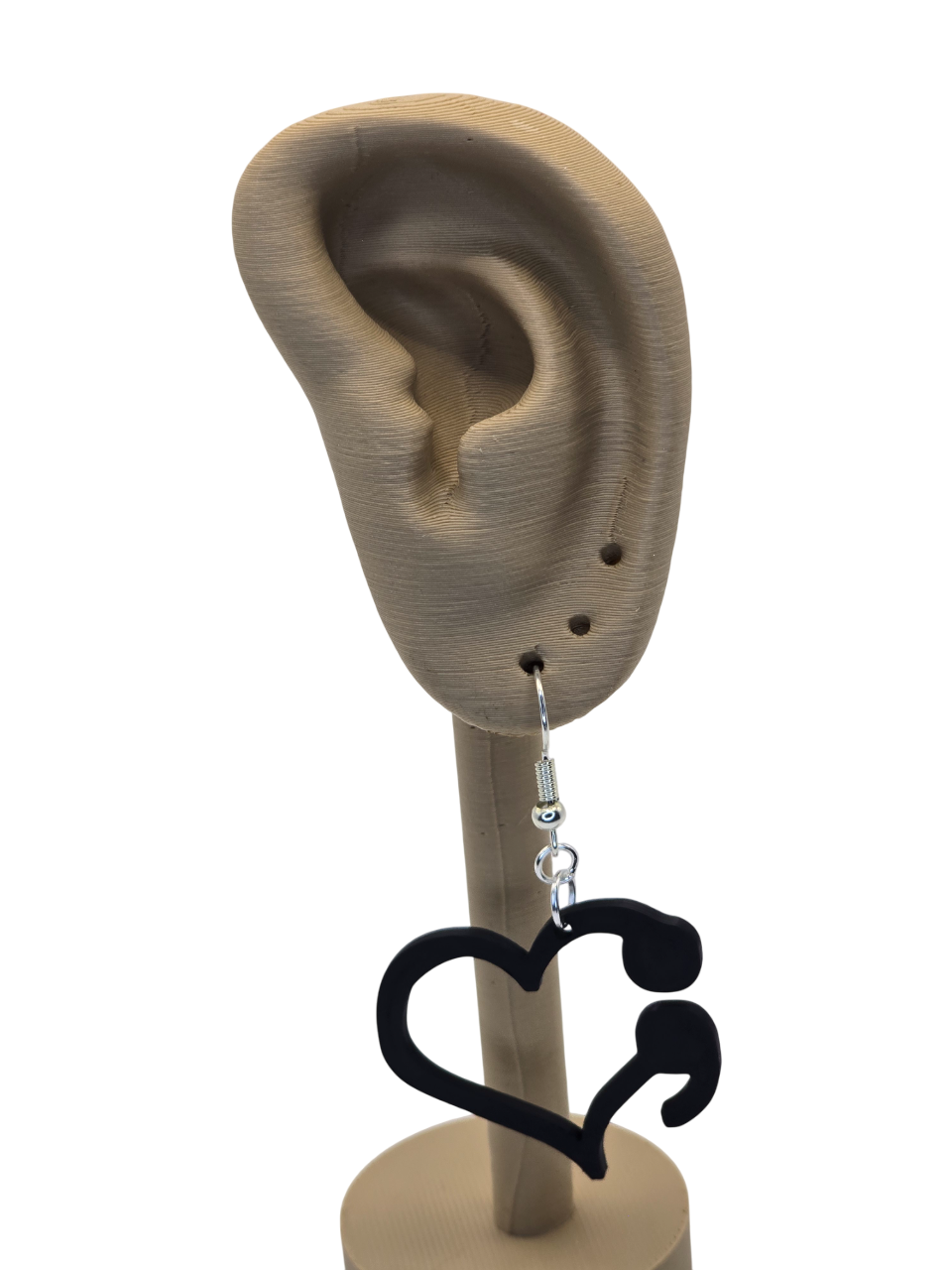 Black heart-shaped earrings on a 3d printed mannequin ear with a white background