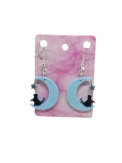 3D printed earrings featuring a black cat sitting on a light blue crescent moon with a silver star.