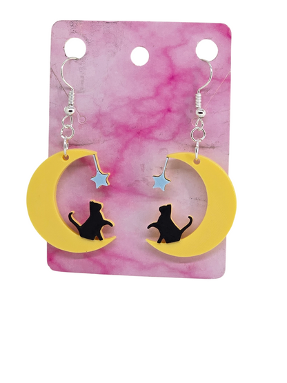 3D printed earrings featuring a black cat sitting on a yellow crescent moon with a blue star.