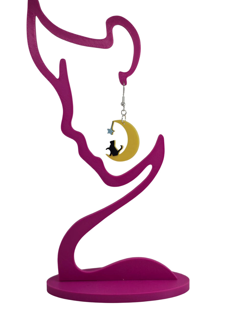 3D printed earrings featuring a black cat sitting on a yellow crescent moon with a blue star on a pink display.
