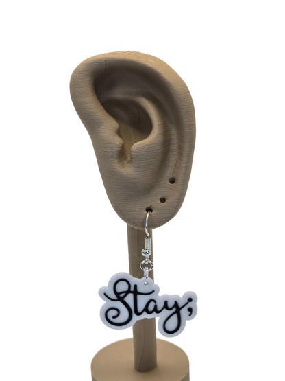 Earring with 'Stay ;' charm displayed on a 3d printed ear stand.