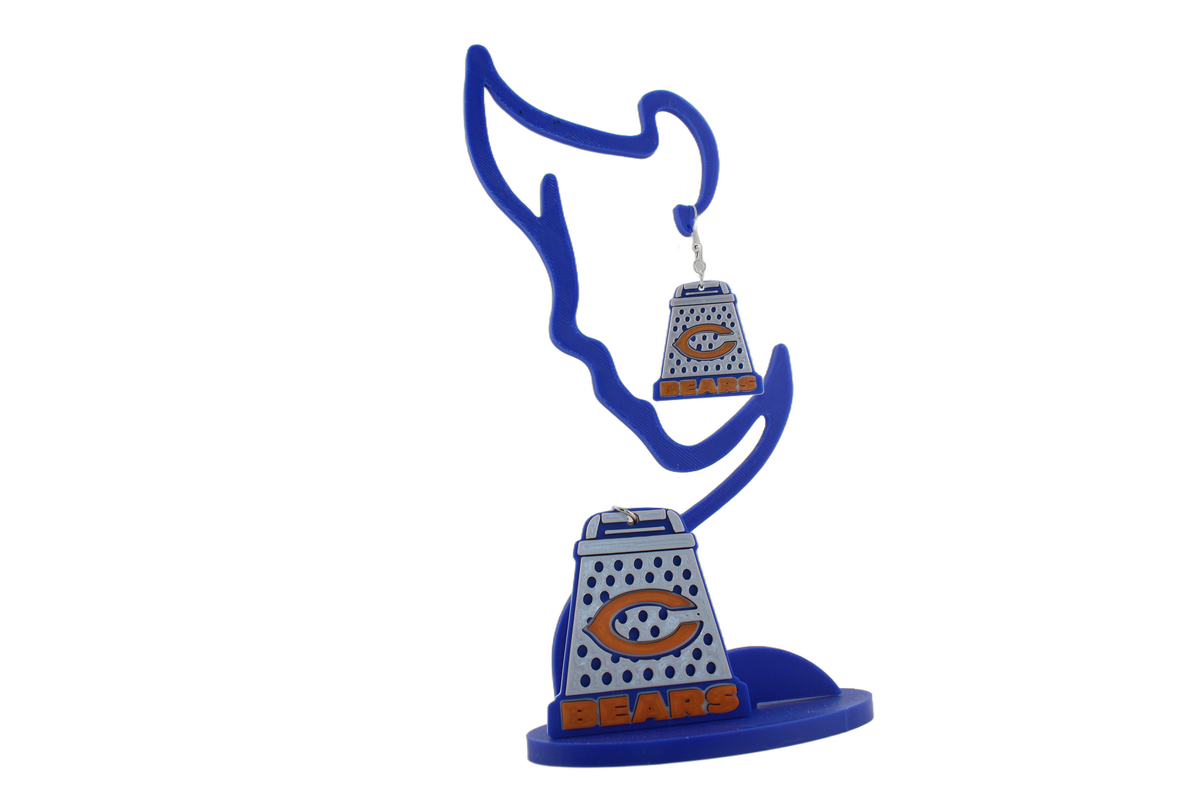 3D printed Chicago Bears cheese grater earrings on a blue display stand, showing the orange C logo and BEARS text detail.