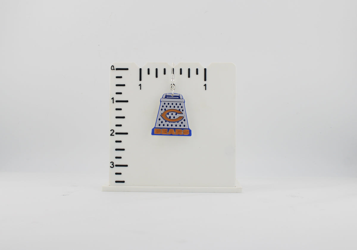 3D printed Chicago Bears cheese grater earring next to a ruler showing approx. 1.25 inch height for size reference.