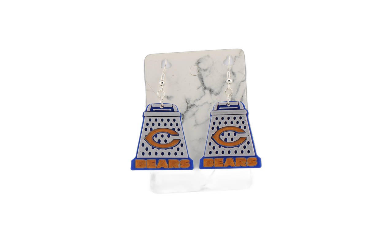 3D printed Chicago Bears cheese grater earrings on a marble-patterned display card, highlighting the blue, white, and orange design.