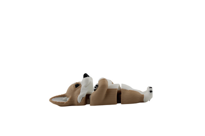 Side profile of a tan and white 3D printed corgi figurine lying flat with its head resting sideways, showing its long ear, articulated waist and white-tipped rear paw, made by Erratically Eccentric Creations.