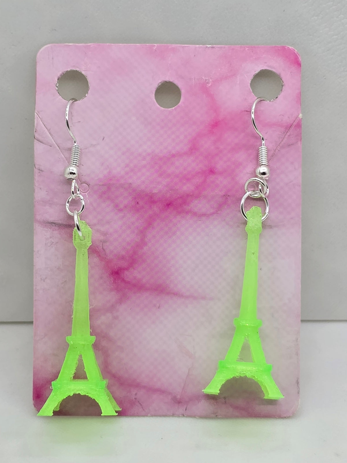 3D printed lime green flexible Eiffel Tower earrings on silver hooks against a pink marble card.