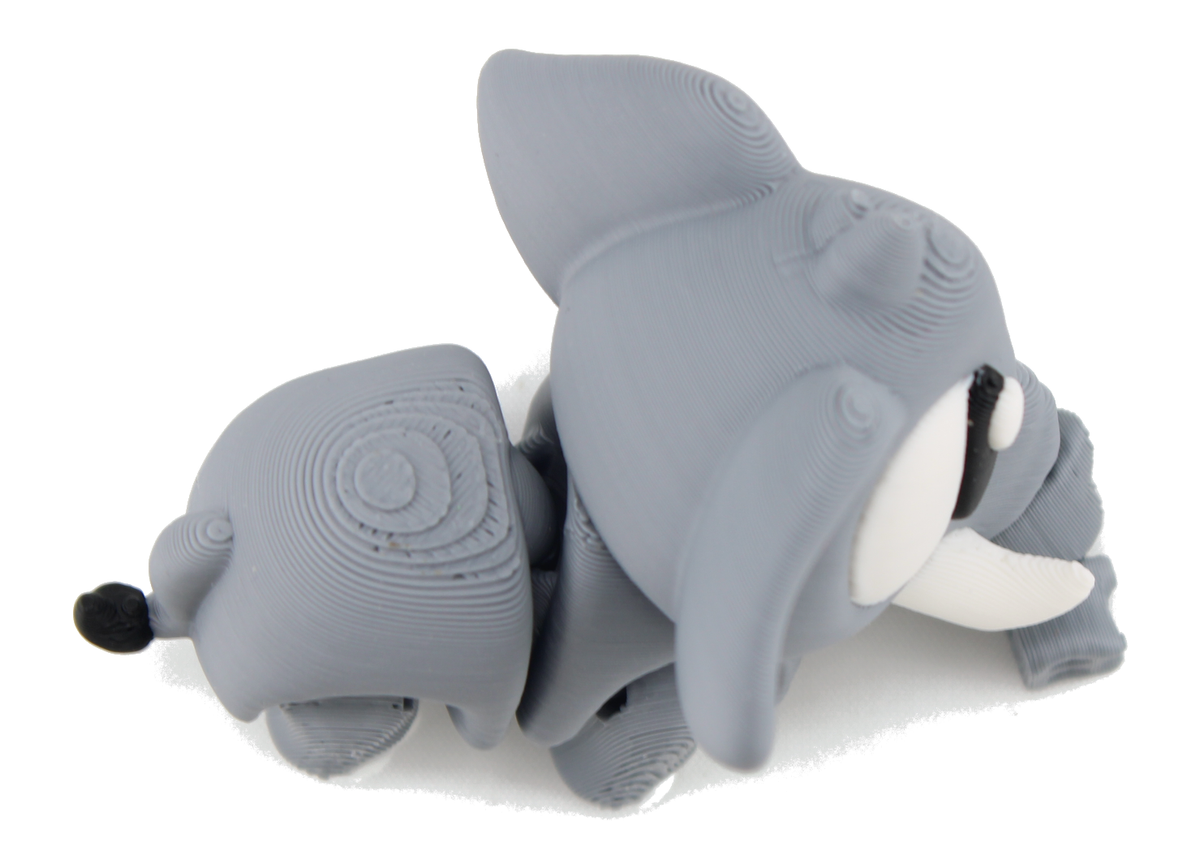 Top-down view of the 3D printed flexi elephant lying down, showing the gray segmented body, big ears and white tusk from above