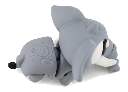 Top-down view of the 3D printed flexi elephant lying down, showing the gray segmented body, big ears and white tusk from above