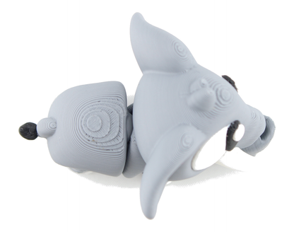 Overhead view of the 3D printed gray baby elephant on its belly, ear lifted, white eye and tusk visible beside the curled trunk