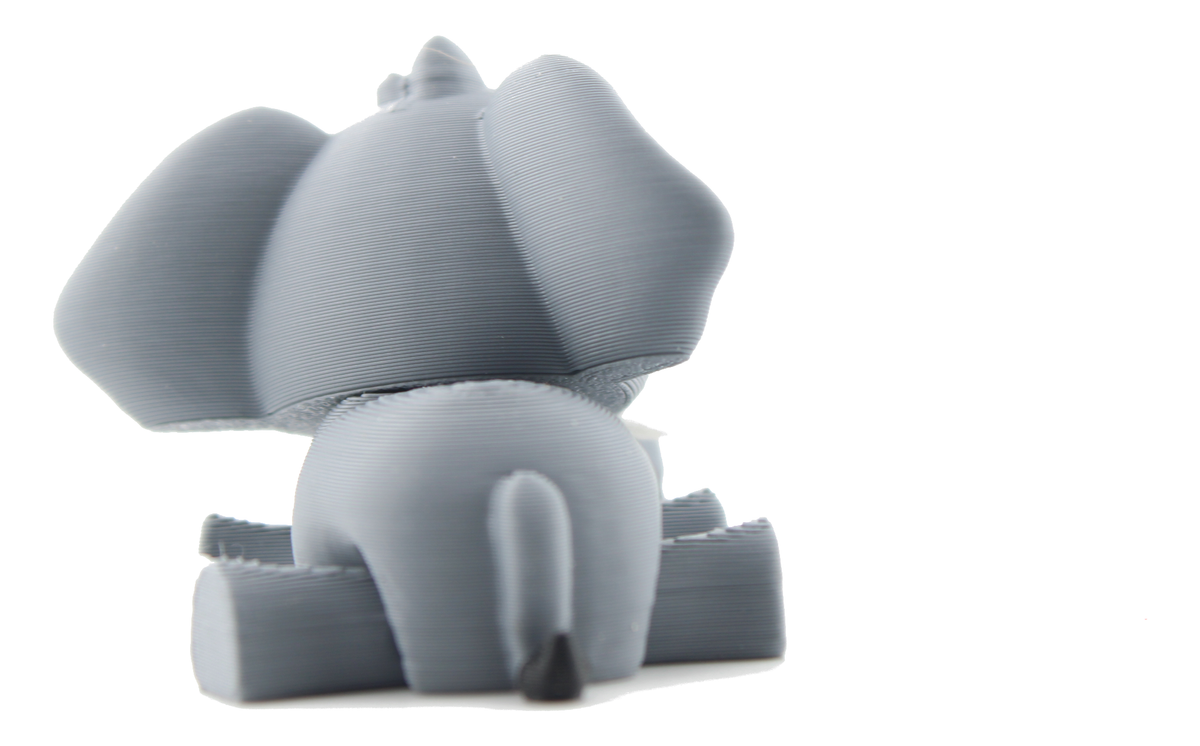 Back view of the 3D printed baby elephant lying down, gray ears spread wide and a thin tail with a black tip