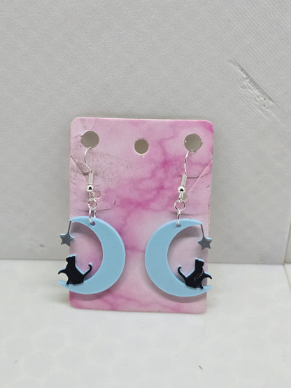 3D printed earrings featuring a black cat sitting on a light blue crescent moon with a silver star.