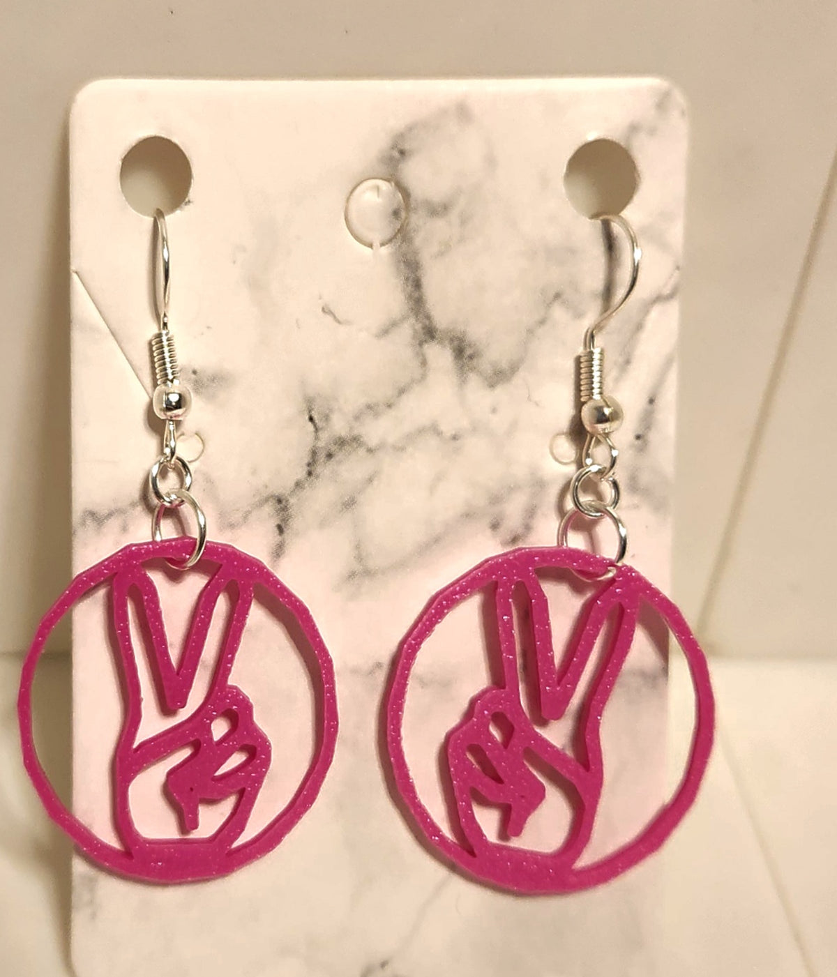 Magenta 3D printed earrings featuring a peace sign hand gesture inside a circle on silver hooks.