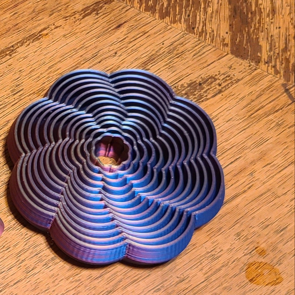 3D printed flower fidget with a blue and purple iridescent silk finish on a wooden surface.