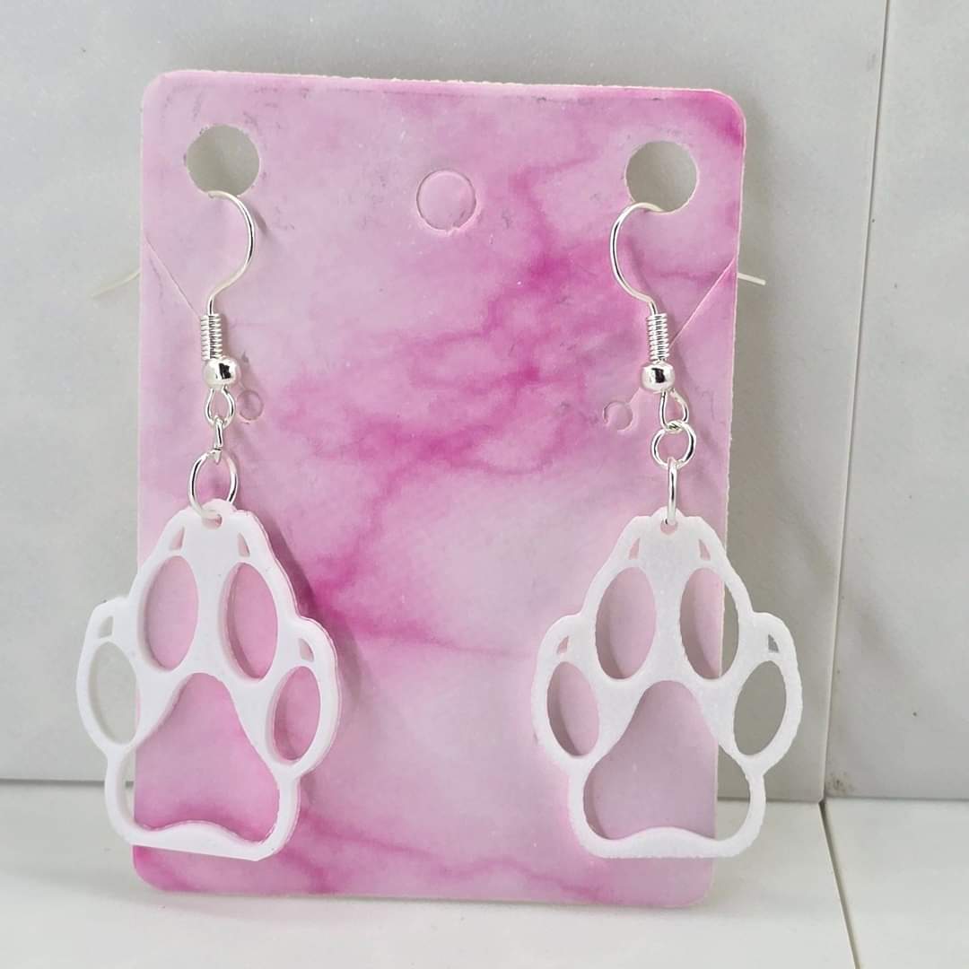 3D printed white hollow wolf paw print dangle earrings with silver-plated hooks on a pink card.